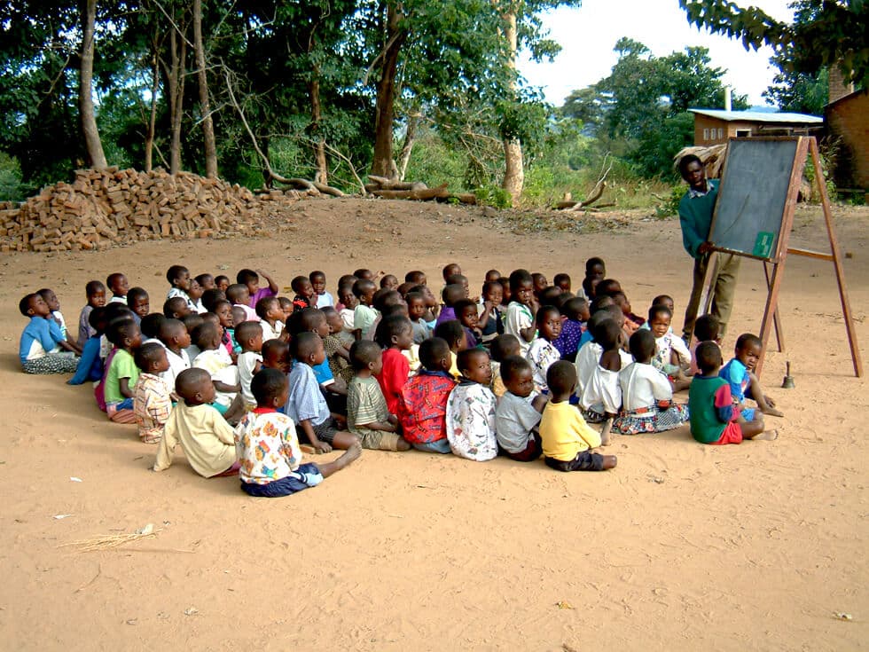 African kids studying under a tree while seated on ground